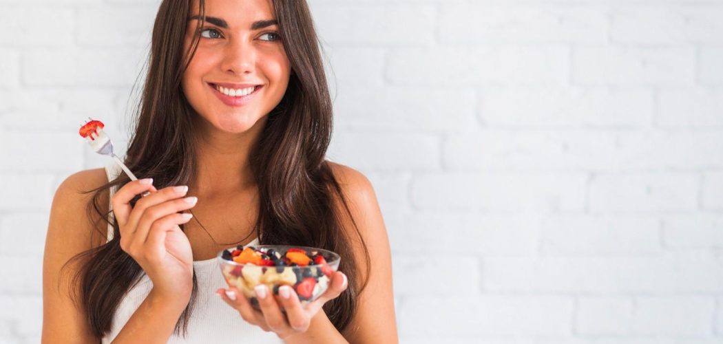 thoughtful-smiling-young-woman-holding-bowl-fruit-salad (1)